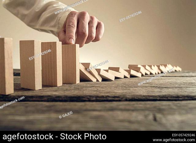 Businessman stopping collapsing wooden dominos with his finger. Conceptual of business crisis solution