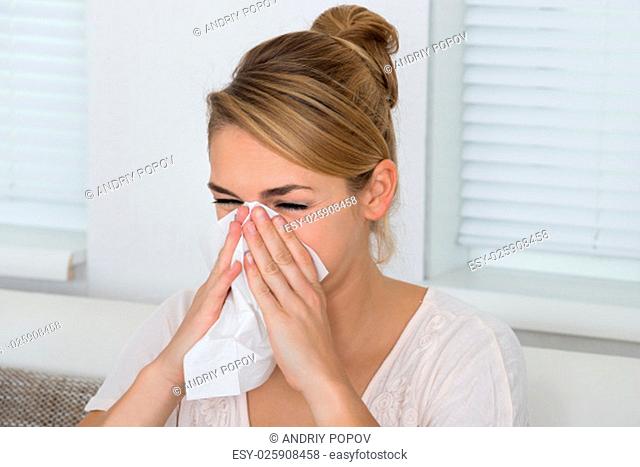 Young woman blowing nose while suffering from cold at home