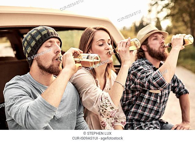 Three people drinking bottled beer in unison