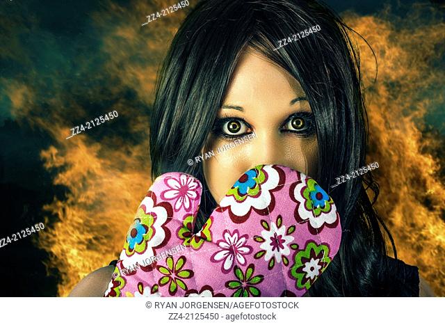 Cooking concept of a woman expressing shock horror with cooking glove to face on kitchen fire background. Bad cook