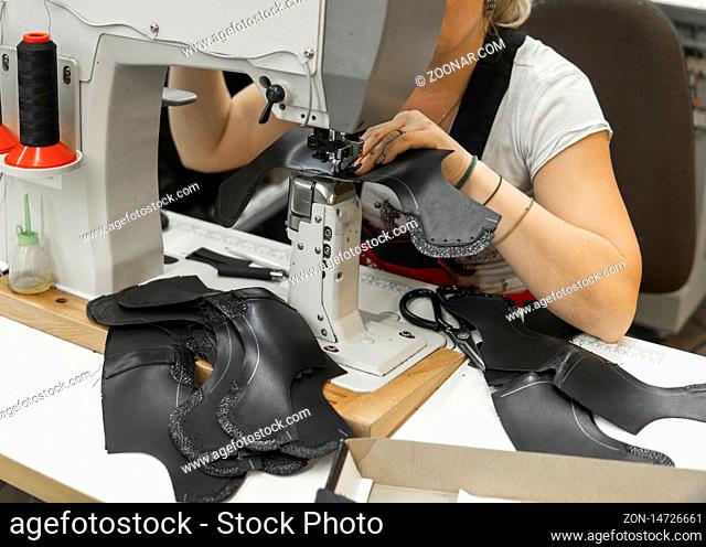 Sewing machine in a leather workshop in action with hands working on a leather details for shoes. Women's hands with sewing machine at shoes factory