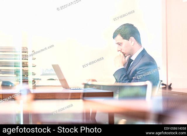 Portrait of successful corporate businessman in bright modern office working on laptop computer. Business and entrepreneurship concept