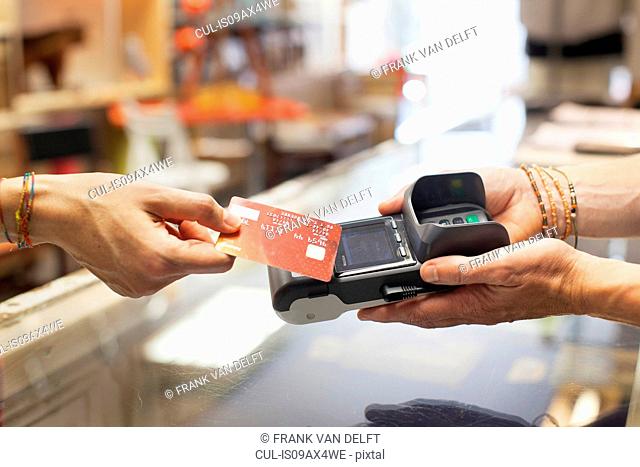 Cropped view of womens hand using credit card to make contactless payment on chip and pin machine