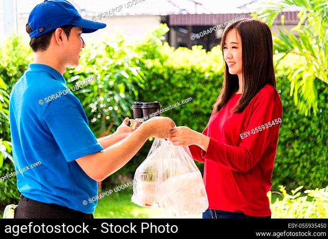 Asian young delivery man in blue uniform he making grocery service giving rice food boxes plastic bags to woman customer receiving front house under pandemic...