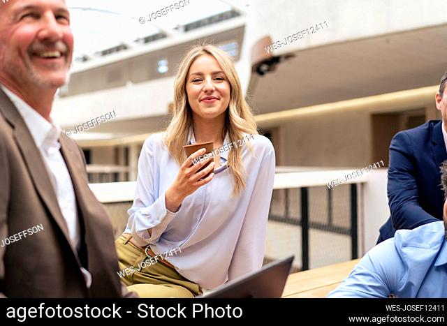 Smiling businesswoman having coffee by colleagues at office