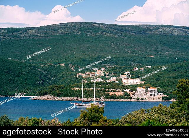 White sailing schooner sails along a blue bay against the backdrop of green mountains and an ancient city. High quality photo