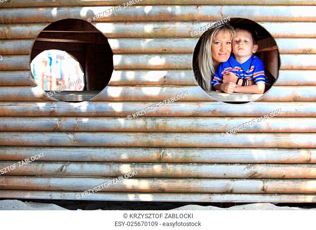 young boy kid with mother or child peeks through hole at playground outdoors at park