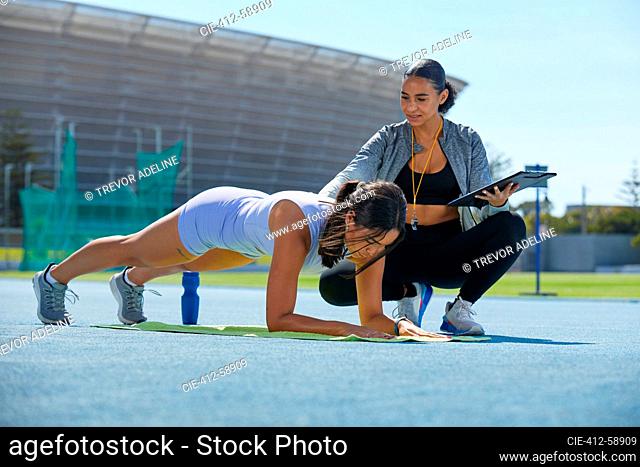 Trainer helping female track and field athlete doing planks on track