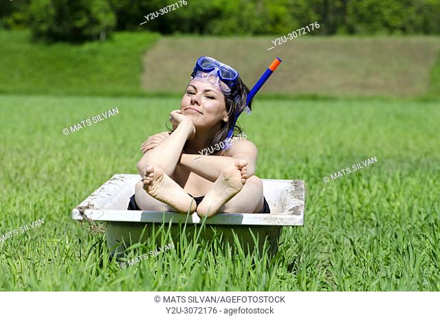 Woman with Diving Mask Sitting in a Bathtub on a Green Field with Grass in Locarno, Switzerland
