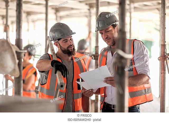 Male builders looking at blueprint on construction site