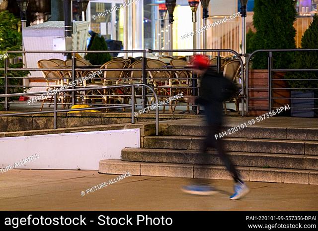 31 December 2021, Hamburg: Early in the morning, a jogger runs along the tables and chairs of a restaurant on Jungfernstieg. Photo: Jonas Walzberg/dpa