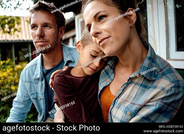 Woman embracing son with eyes closed by man at backyard