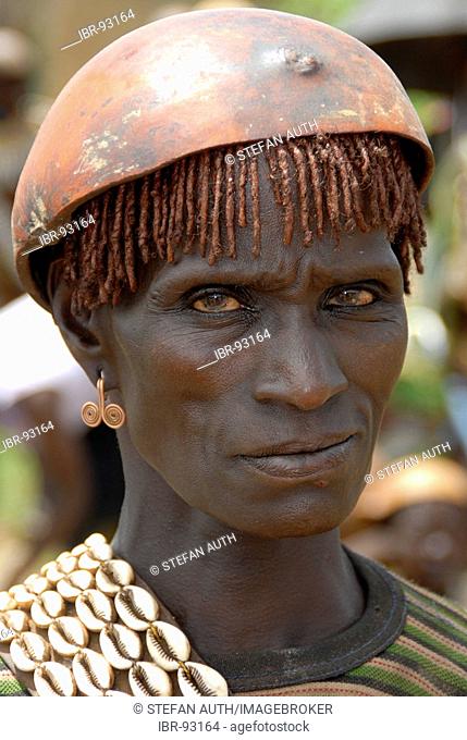 Portrait austere looking woman wearing a chain of kauri mussels and a kalabasse on her head on the market of Keyafer Ethiopia