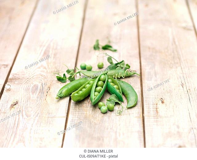 Still life of green peas in pods with pea shoots on wooden table
