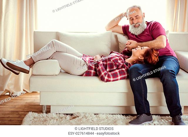 Happy mature man looking at beautiful smiling woman lying on sofa