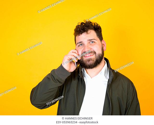 cool man with smartphone, black beard and black hair is posing in front of orange background and doing different expressions