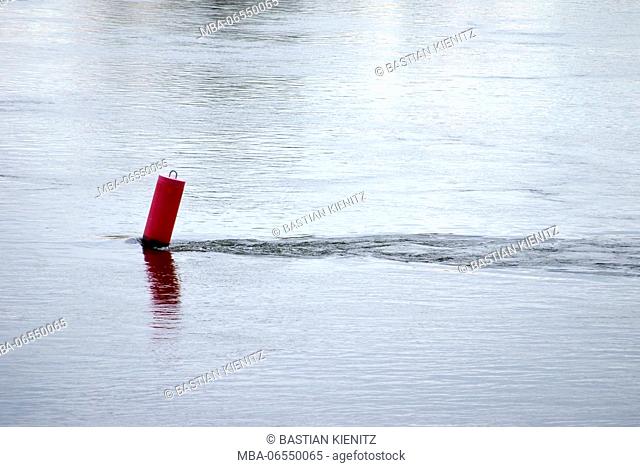 A red signal buoy is bent by the river flow
