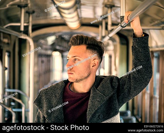 Young handsome man riding on tram or old bus in city, wearing winter clothes