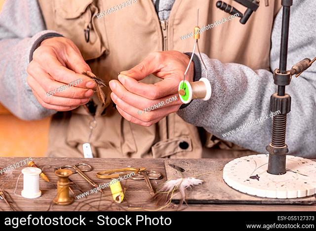 Man making trout flies. Fly tying equipment and material for fly fishing preparation