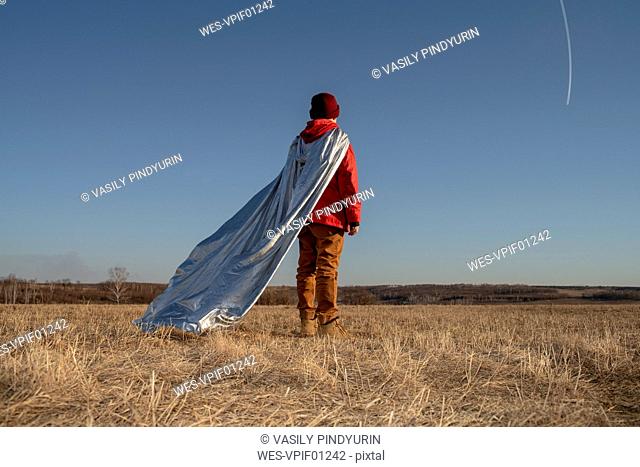 Rear view of boy dressed up as superhero looking at vapour trails in the sky