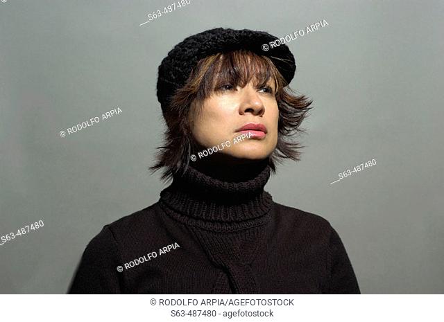 Portrait of a brunette latin woman wearing black turtleneck sweater and hat looking away