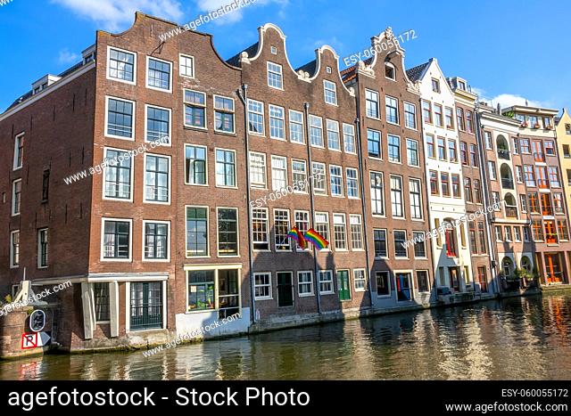 Netherlands. Sunny day on the Amsterdam canal. Traditional houses and two flags of the LGBT community on the facade
