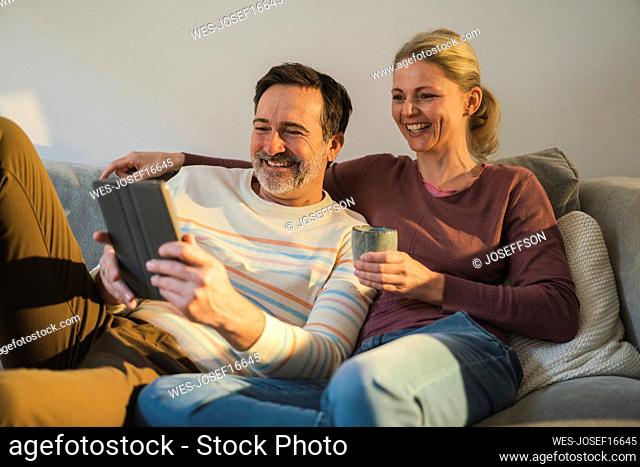 Happy mature couple watching tablet PC sitting on sofa at home