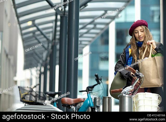 Young woman placing groceries in bike cart in city