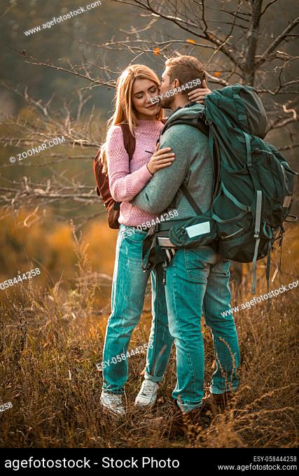Couple In Love Rest Stopping On The Edge Of Cliff, Young Backpackers Hug And Kiss On Background Of Beautiful Autumn Nature