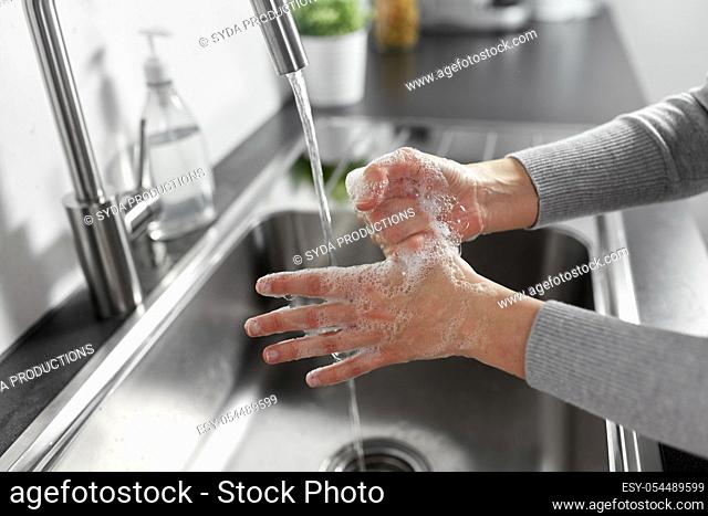 woman washing hands with liquid soap in kitchen