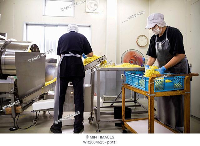 Workers in aprons and hats collecting freshly cut noodles from the conveyor belt to package and sell