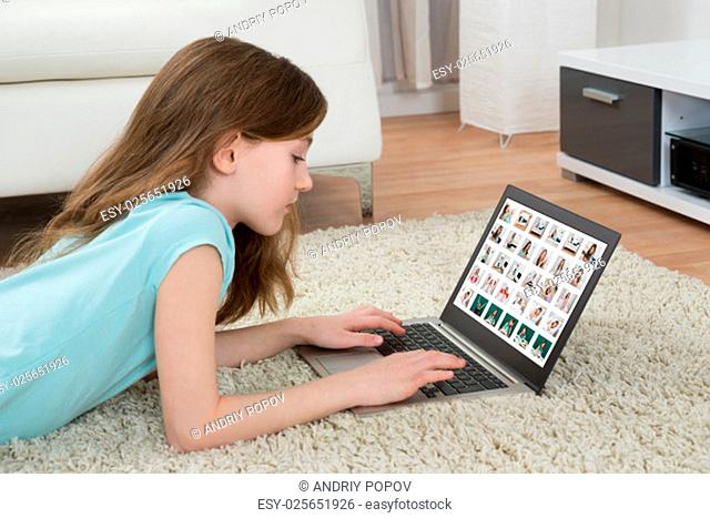 Girl On Carpet Looking At Pictures On Laptop In Living Room