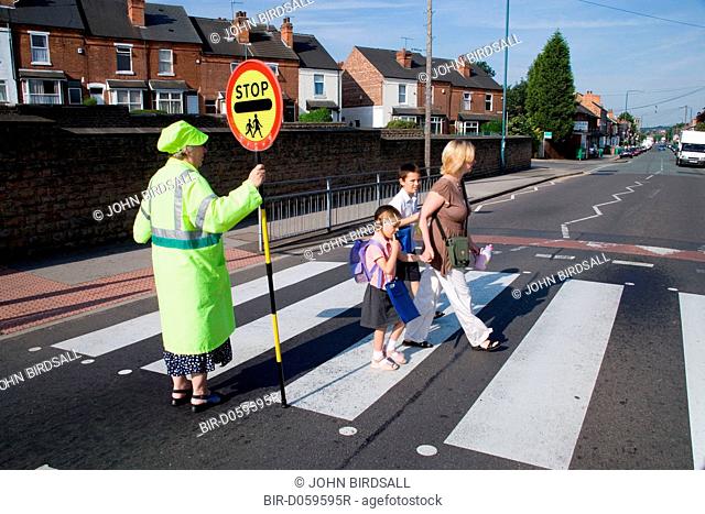 Mother walking children to school crossing a zebra crossing