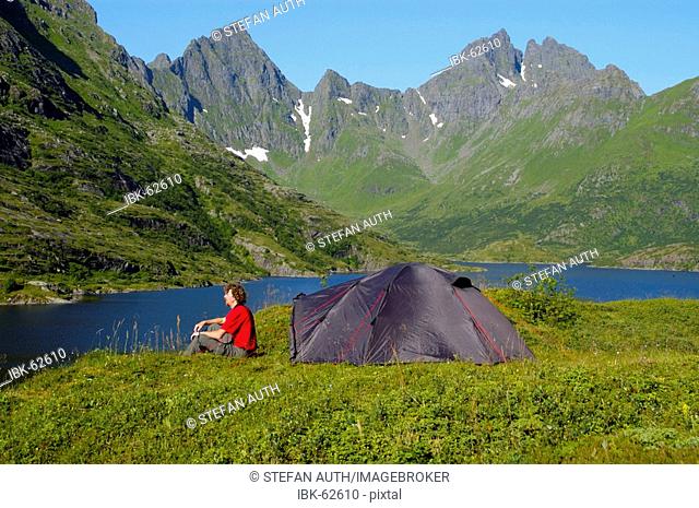 MR Young man sits at his tent in the wilderness of Moskenesoya with Agvatnet and Mannen Lofoten Norway