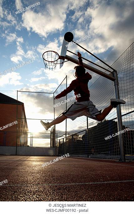 Teenager playing basketball, dunking against the sun