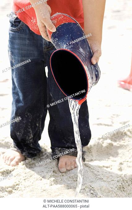 Child pouring water out of rubber boot at the beach
