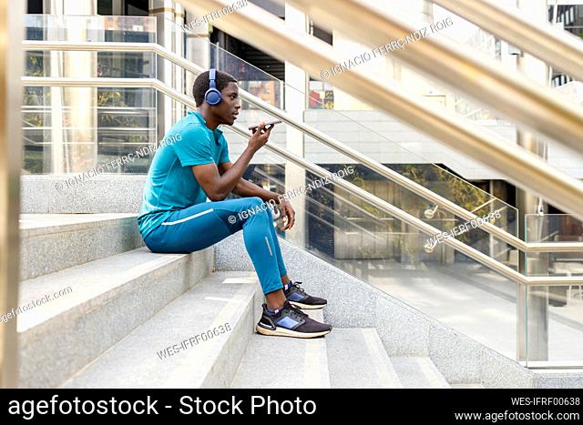 Man wearing headphones sending voicemail while sitting on staircase