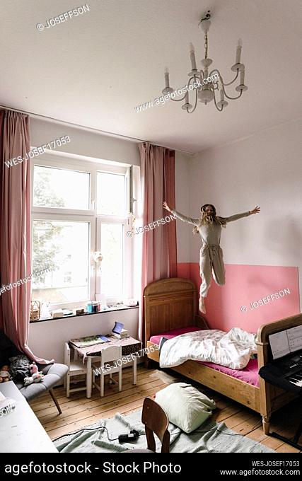Girl with arms outstretched jumping on bed at home