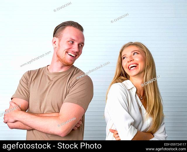 Young caucasian couple stand with arms folded, made eye contact, and smile at each other