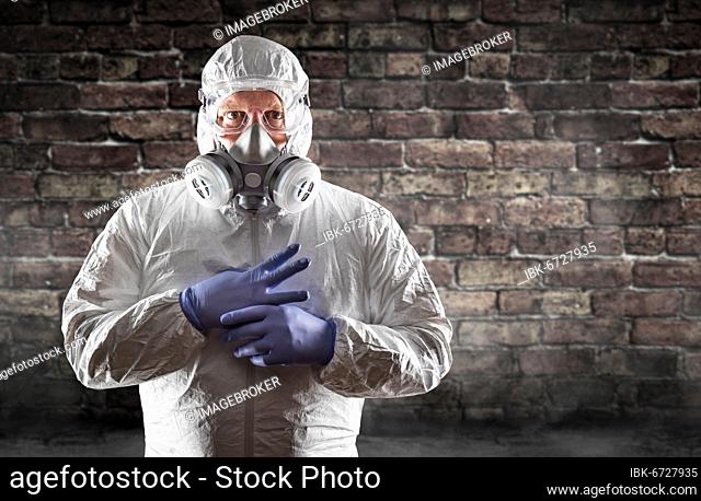 Man wearing hazmat suit, protective gas mask and goggles against brick wall
