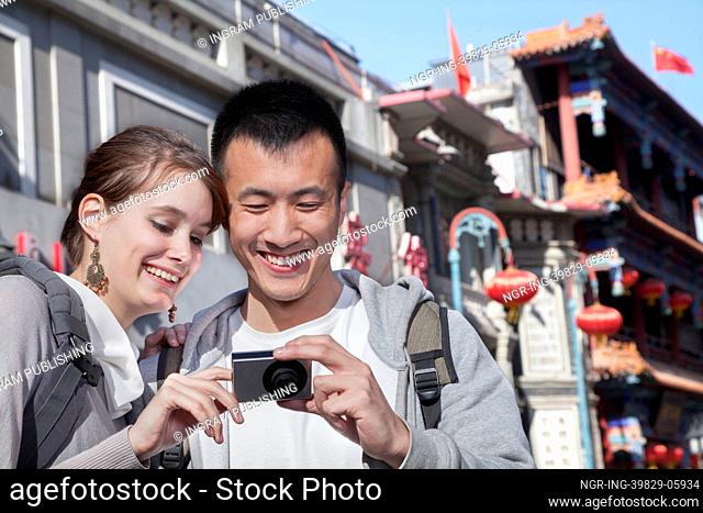 Young couple sightseeing, looking at digital camera