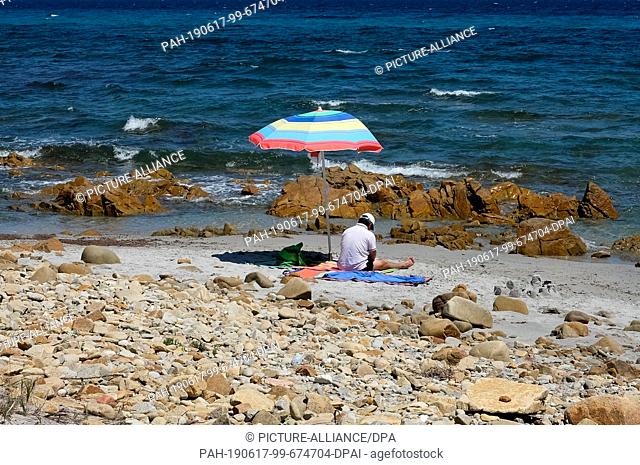 05 June 2019, Italy, Nuoro: A man has sat under a parasol on a beach in the National Park di Bidderosa in the Gulf of Orosei
