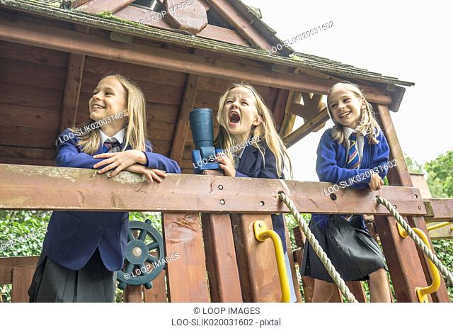 Three girls in school uniform stand together on wooden playground apparatus