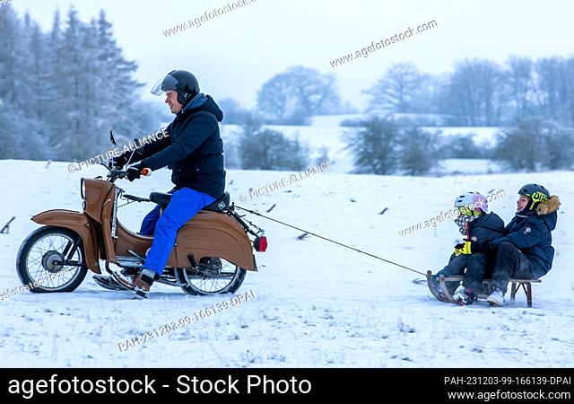 03 December 2023, Mecklenburg-Western Pomerania, Pokrent: A family is out and about in the snow on a moped with a sledge attached