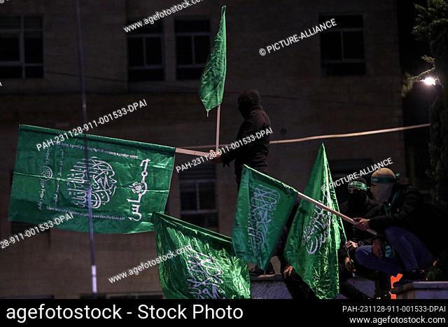 28 November 2023, Palestinian Territories, Ramallah: Men hold Hamas flags as they gather to welcome Palestinian prisoners released from Israeli jails