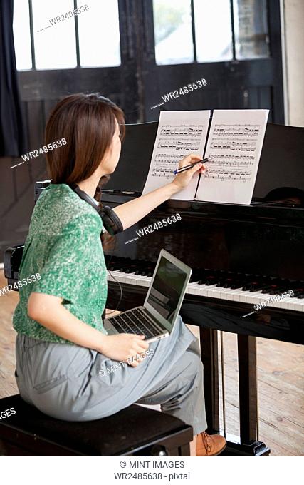 Young woman sitting at a grand piano in a rehearsal studio, annotating sheet music