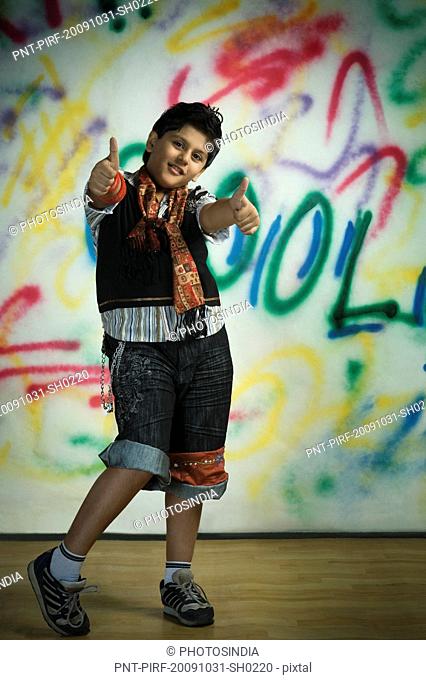 Boy showing thumbs up sign in front of a graffiti covered wall