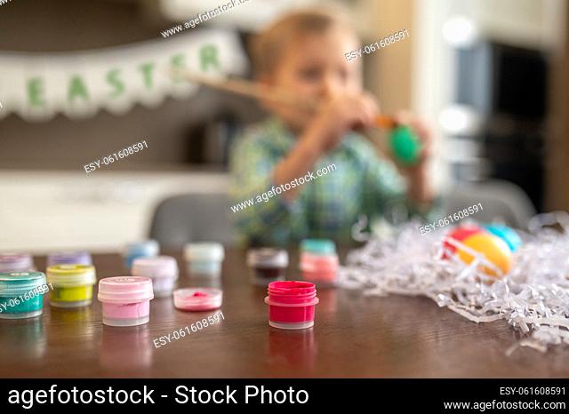 Defocused photo of a busy kid sitting at the table among numerous transparent plastic food coloring bottles
