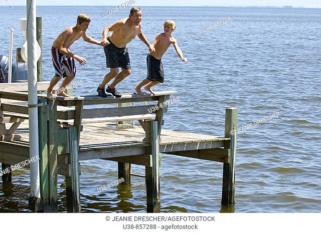 Grandfather jumping from dock with grandsons