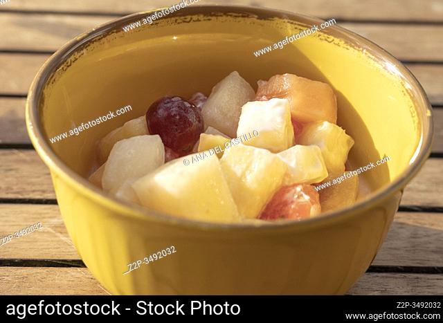 Top view of white bowl full of fruit salad containing strawberries, grapes, orange, kiwi, pineapple and apple